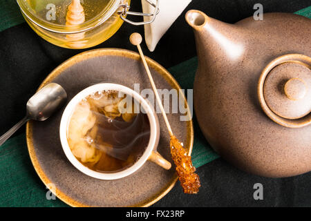 Una tazza di tè caldo su un tavolo con teiera e miele. Il latte è la miscelazione con tè Shot dal di sopra Foto Stock