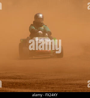 Uomo con casco e tuta guida tosaerba motore emergente dalla nube di polvere rossa sulla via insolito Australian motor racing sport Foto Stock