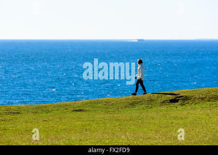 Kaseberga, Svezia - Aprile 1, 2016: Donna camminando sulla cima di una collina lungo la costa che si affaccia sul mare e la visione di una barca ho Foto Stock