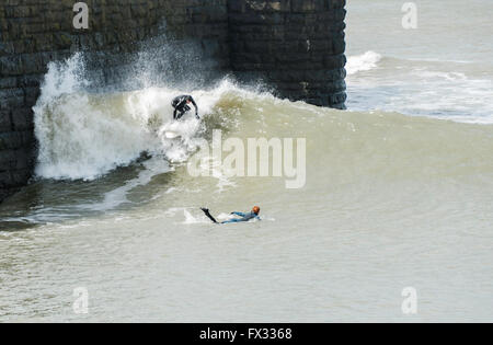 Aberystwyth, Ceredigion, West Wales, 10 aprile 2016 UK Meteo: Due Surfers prendere vantaggio della maggiore rispetto al normale alta marea a 5.48m, l'aumento di vento e la massiccia gonfiarsi per navigare pericolosamente vicino lungo la banchina a parete come la gente guarda a scattare foto e video godendo il vento ancora chiaro meteo. Credito: Veterano Fotografia/Alamy Live News Foto Stock