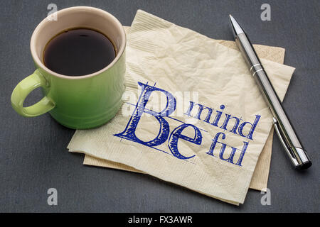 Essere consapevoli - scrittura su un tovagliolo con tazza di caffè contro di ardesia grigia sullo sfondo di pietra Foto Stock