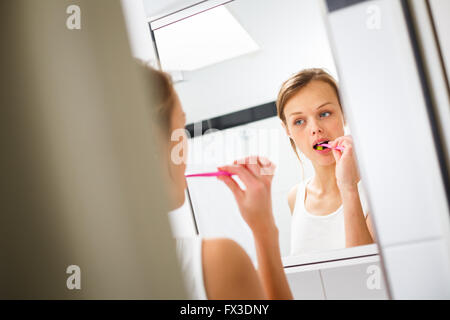 Bella femmina spazzolare i suoi denti nella parte anteriore dello specchio al mattino Foto Stock