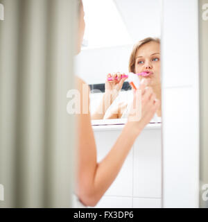 Bella femmina spazzolare i suoi denti nella parte anteriore dello specchio al mattino Foto Stock