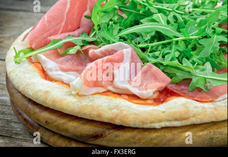 Pizza con insalata di rucola e prosciutto su piatto di legno Foto Stock