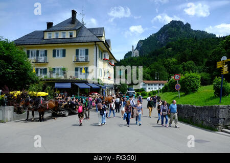 I turisti nel villaggio bavarese di Hohenschwangau, vicino a Füssen in Germania, con il Castello di Neuschwanstein sulla collina al di là. Foto Stock