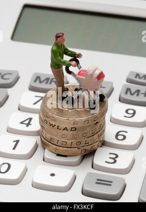 Un unico maschio statuetta in miniatura genitore con una carrozzina permanente sulla libbra di monete e di una calcolatrice Foto Stock