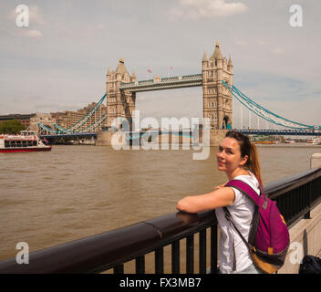 Una giovane donna in primo piano guardando la telecamera con il Tower Bridge in background in una giornata di sole nella città di Londra,UK Foto Stock