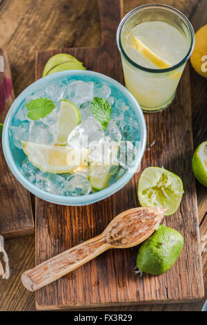 Ingredienti per la limonata fresca per le calde giornate estive, lime e limoni, ghiaccio e menta in vaso vintage. Foto Stock