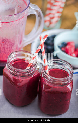Due vasi con berry smoothie, frutta fresca in background. Pulire il mangiare e il concetto di dieta Foto Stock