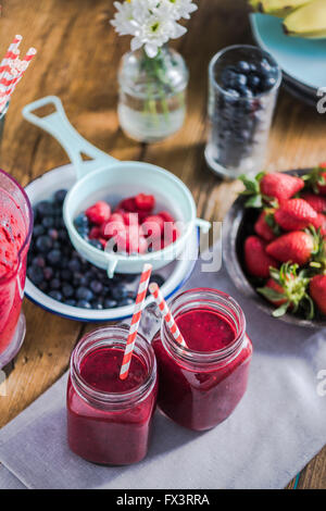 Due vasi con berry smoothie, frutta fresca in background. Pulire il mangiare e il concetto di dieta Foto Stock