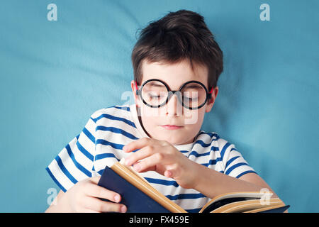 A sette anni di età bambino giacente con libro Foto Stock