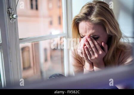 Donna seduta sul davanzale, guardando fuori della finestra piangendo Foto Stock