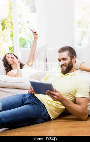 Uomo con tavoletta digitale mentre la donna prendendo selfie dal telefono cellulare Foto Stock