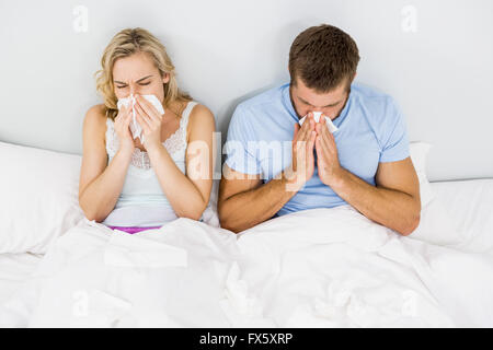 Giovane che copre il naso mentre starnuti sul letto Foto Stock