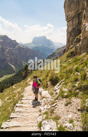 Donna escursionismo nelle Dolomiti, in piedi in scale guardando la telecamera e il paesaggio con le alte montagne sullo sfondo, Foto Stock