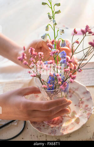 Donna ispanica disponendo dei fiori in tazza di vetro Foto Stock