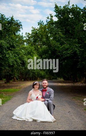 Sposa e lo sposo il giorno delle nozze seduti insieme in una strada di ghiaia di riposo. Foto Stock