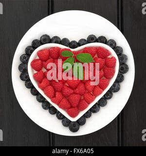 Lampone e mirtillo Frutta in un cuore ciotola sagomata su un bianco piatto rotondo su sfondo nero. Foto Stock