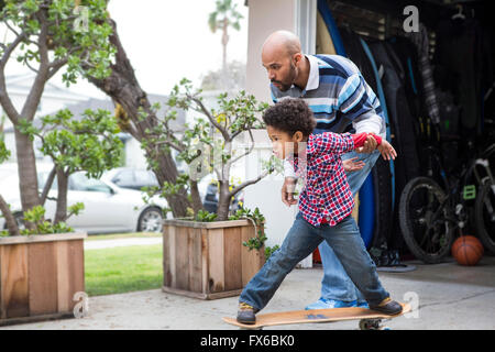 Razza mista padre figlio di insegnamento a cavalcare skateboard all'aperto Foto Stock