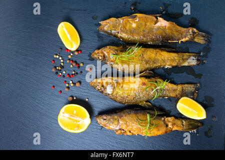 Vista dall'alto di fritto tinca pesce servite con idrocarburi aromatici di rosmarino e di limone e peperoni secchi su sfondo di ardesia, close up Foto Stock