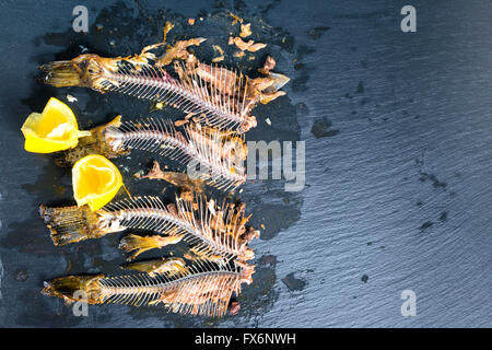 Top down di pesce le ossa dello scheletro senza capi, limone spremuto su sfondo di ardesia, close up Foto Stock