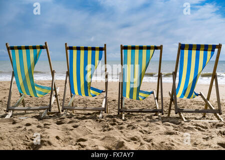 Una fila di 4 blu e giallo listati di sedie a sdraio al vento sulla spiaggia di Bournemouth, Regno Unito Foto Stock