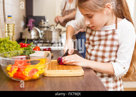 Cucina di famiglia dello sfondo. Piccola ragazza il taglio di cipolla insalata di preparazione al banco di cucina Foto Stock