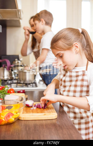 Ragazza adolescente cucinare insieme con la sua famiglia in cucina. Ragazza caucasica cipolla di taglio per insalata famiglia sullo sfondo di cottura Foto Stock