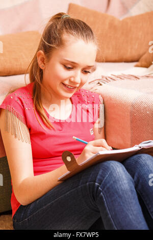 Giovani felici sorridente ragazza adolescente iscritto nel notebook diario seduto sul pavimento Foto Stock