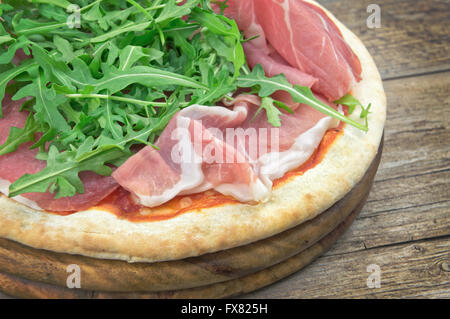 Pizza con insalata di rucola e prosciutto su piatto di legno Foto Stock