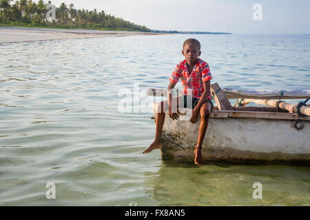 Un ragazzo si siede sulla poppa di una piccola dhow sulla costa di Zanzibar Africa orientale Foto Stock