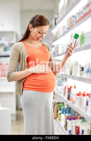 Felice donna incinta scegliendo lozione in farmacia Foto Stock