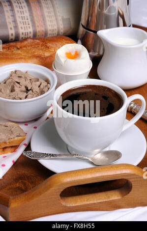 La colazione su un vassoio con una tazza di caffè e toast con patè di fegato, soft-uova sode e un giornale Foto Stock
