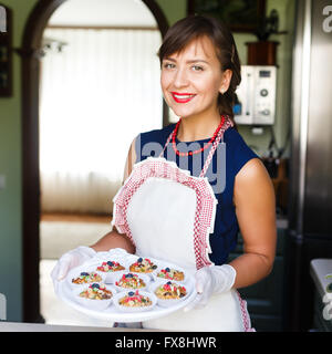 Giovane donna tenendo un vassoio con tortine alla cucina Foto Stock