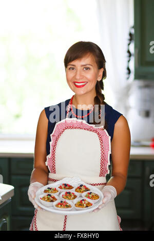 Giovane donna tenendo un vassoio con tortine alla cucina Foto Stock