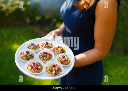 Giovane donna tenendo un vassoio con tortine in giardino Foto Stock