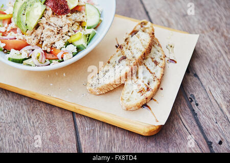 Fresca baguette affettata al fianco di un insalata fresca sulla tavola di legno Foto Stock