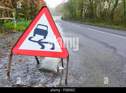 Strada sdrucciolevole triangolare segno di avvertimento su una strada allagata nel Regno Unito. Foto Stock