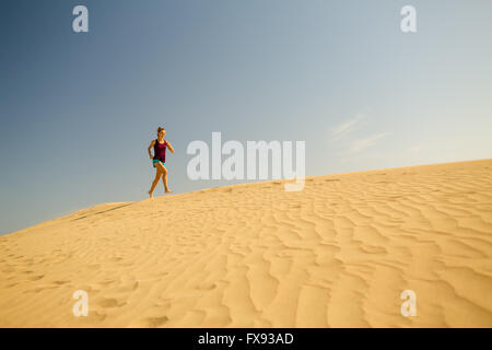 Giovane donna in esecuzione sulla splendida ispirazione dune del deserto su soleggiate giornate estive. Femminile della formazione e del lavoro, jogging Foto Stock