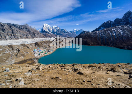 Vista del lago e del villaggio di Gokyo Da Gokyo Ri, il ghiacciaio Ngozumba e montagne coperte di neve in lontananza, Gokyo Foto Stock