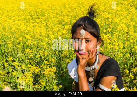 Ritratto di una giovane donna di locali appartenenti alla tribù Tharu, seduti in un giallo senape campo, Sauraha, Chitwan, Nepal Foto Stock