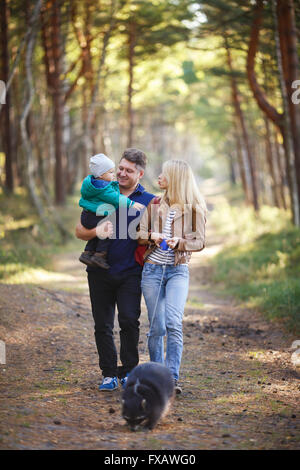 La famiglia felice con raccoon camminando in una foresta Foto Stock