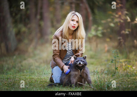 Ritratto di attraente giovane donna con raccoon in una foresta Foto Stock