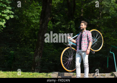 Un potente uomo appeso la sua bici sulla sua spalla, rimanendo su scale, sguardo lontano. Foto Stock