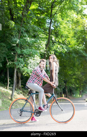 Un bel paio di divertirsi su una bicicletta sotto la presenza di alberi verdi e sole estivo Foto Stock