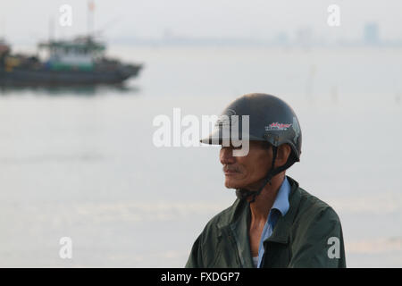 Uomo vietnamita con il casco in moto nella parte anteriore della barca da pesca e sul Mare del Sud della Cina a Danang beach, Vietnam Foto Stock