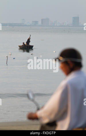 Uomo vietnamita con moto; coracle boat & skyline a Danang beach, Vietnam Foto Stock