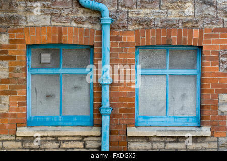 Pietra e mattoni casa parete con finestre blu e drainpipe astratta. Glastonbury, Somerset, Inghilterra Foto Stock