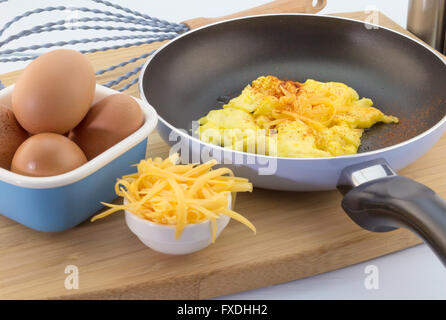 Focus su soffici uova strapazzate in padella condito con pepe di Caienna e il formaggio cheddar leggera profondità di campo Foto Stock