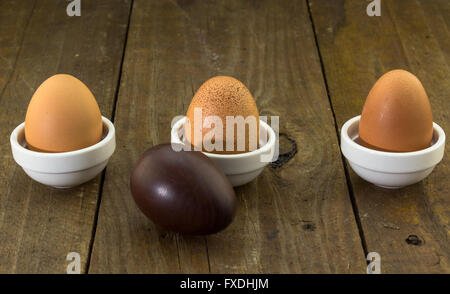 Foto concettuale di tre uova di gallina in una fila su legno rustico sfondo con un legno scolpito uovo in primo piano Foto Stock